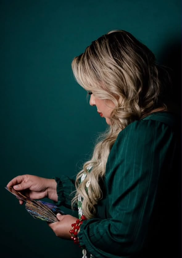 Mulher de perfil segurando um leque de cartas de tarô, vestida de verde